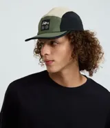Gorra tipo 5 panel confeccionada en microfibra de poliamida, con diseño de bloques de colores en beige, negro y verde oliva. Presenta visera recta, cierre posterior ajustable y etiqueta frontal con gráfico y frase Stay Grounded.