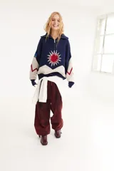 Sweater de punto de algodón con cuello polo y cierre frontal. Presenta un diseño con intarsia de sol y montañas en tonos azul, blanco y rojo, con detalle de parche en la manga.