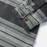 Camisa de franela a rayas horizontales en tonos grises, con cuello clásico, manga larga, cierre frontal con botones marrones, dos bolsillos con botón en el pecho y puños abotonados.