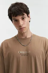 Remera de manga corta color gris oscuro, con escote redondo y ajuste regular. Presenta un estampado frontal con el texto "MISTRAL KAMIOKA NEW TRIAL SINCE 1976 // NLD".