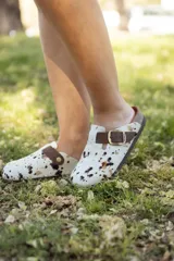 Zueco con capellada de pelo de vaca con manchas marrones y negras sobre base blanca, plantilla anatómica de cuero y hebilla lateral ajustable.