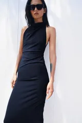 Vestido largo de corte fluido con cuello halter y espalda descubierta. Presenta un detalle de drapeado lateral y bajo recto.