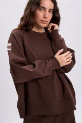Sudadera de cuello redondo y manga larga en color marrón, con diseño holgado y detalle de etiqueta en la manga.