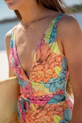 Malla enteriza con escote en V profundo, tirantes anchos y lazo ajustable en la cintura. Presenta un estampado floral vibrante con tonos naranjas, rosas, celestes y verdes.