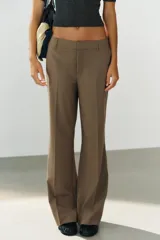 Pantalón de tiro bajo color marrón, con bolsillos frontales, falsos bolsillos traseros de vivo y cierre delantero con cremallera y gancho metálico.