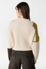 Sweater de punto con diseño de bloques de color en tonos crema y marrón. Presenta cuello redondo, mangas largas y una silueta holgada con detalle de placa metálica decorativa en el lateral.