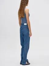 Pantalón de denim color marrón, de tiro alto y calce ochentoso con terminación estilo oxford. Cuenta con apliques metálicos decorativos alrededor de los bolsillos y a lo largo de las costuras exteriores.