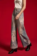 Pantalón jean de tiro medio y corte ancho, con estampado artístico en tonos celestes y blancos.