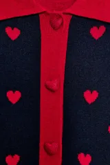 Chaqueta de punto jacquard en color azul marino con estampado de corazones rojos. Presenta cuello de solapa, manga larga y cierre frontal con botones rojos en forma de corazón. Los puños, el cuello y el bajo son de color rojo liso.