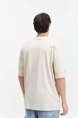 Remera de manga corta color gris oscuro, con corte holgado, hombros caídos y escote redondo. Presenta un logo estampado en el pecho con la inscripción "GALLERY DEPT." en color naranja.