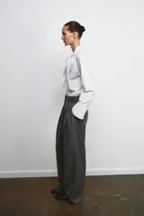 Pantalón de tiro medio con pinzas frontales, confeccionado en tejido con viscosa. Presenta cintura con trabillas, bolsillos laterales y cierre frontal con cremallera, botón y ganchos metálicos.