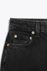 Jeans de mujer, tiro alto, color azul medio con efecto desgastado (lavado claro en muslos y oscuro en bordes). Corte recto y ancho (mom fit) con cinco bolsillos y cierre frontal de botón y cremallera.