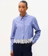 Camisa cropped azul con rayas diplomáticas blancas, cuello clásico, mangas largas y detalle de encaje blanco aplicado en el borde inferior.