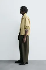 Cazadora de tejido con algodón, color amarillo pálido, con cuello solapa y cierre frontal de cremallera. Presenta bolsillos frontales de vivo y bajo ajustable con elástico en los laterales.