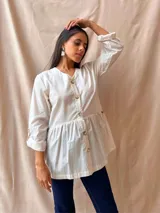 Camisa color crudo con cuello en V, abotonada al frente, con mangas 3/4 con botón para sujetar y corte evasé.