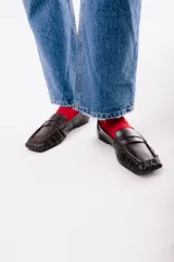 Mocasines de cuero color marrón oscuro, con diseño clásico de tira en el empeine, costuras fruncidas alrededor de la puntera cuadrada y suela plana.