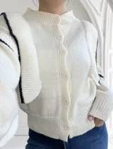 Cárdigan tejido color crudo con cuello redondo, cierre frontal con botones y mangas abullonadas con puños acanalados y detalle de rayas negras.