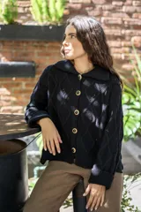 Saco tejido de punto con diseño de ochos y trenzas, color negro. Presenta cuello estilo camisero, cierre frontal con botones tipo joya, mangas holgadas y silueta oversize.