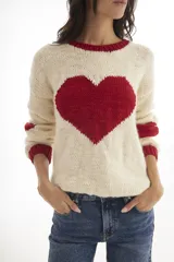 Buzo de tejido de punto artesanal, color crema con un gran corazón negro estampado en el centro y detalles de franjas negras en las mangas. Presenta cuello redondo y puños acanalados.