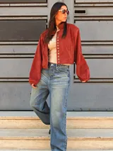 Campera tipo bomber color bordó, confeccionada en gamuza, con cierre frontal y una hilera de botones metálicos decorativos a lo largo de la solapa. Presenta mangas largas con puños holgados y un diseño de corte oversize.