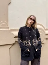 Saco de punto gris con diseño geométrico en color amarillo, cierre frontal con botones, cuello redondo y bordado de corazón pequeño en el pecho.