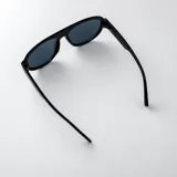 Lentes de sol tipo aviador con armazón negro de policarbonato y detalles metálicos dorados en las patillas. Lentes oscuros con filtro UV400.