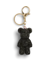 Llavero de metal con acabado en zinc, con un dije en forma de oso de peluche cubierto de cristales negros. Incluye un aro y un mosquetón dorados.