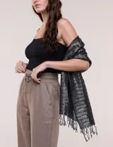Pashmina rectangular de caída fluida, color negro con hilos metalizados que forman líneas horizontales plateadas y terminación de flecos finos en los extremos.