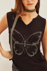 Musculosa negra con escote en V y aplique de mariposa hecho con tachas plateadas. Se complementa con un accesorio tipo choker/collar largo de cuentas plateadas.