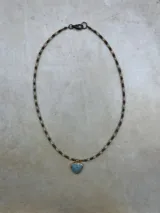Gargantilla delicada compuesta por pequeñas piedras semipreciosas facetadas en tonos oscuros y dorados, con un dije central en forma de corazón de piedra natural negra enmarcado en metal.