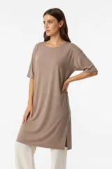 Remera de corte holgado y largo tipo vestido, con cuello redondo y mangas cortas. Presenta un diseño minimalista con aberturas laterales en el ruedo.