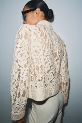 Blazer de encaje con cuello redondo, manga larga con puños y cierre frontal con botones. Presenta un diseño estructurado con bajo recto.