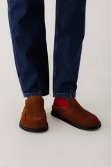 Zueco de cuero color marrón oscuro, con costuras decorativas en hilo rojo en el empeine y suela plana de goma.