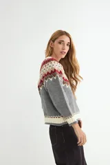 Buzo de punto con diseño de jacquard en el canesú, cuello redondo y mangas largas. Presenta un patrón geométrico multicolor en tonos crema, mostaza, bordó y azul marino sobre una base crema.