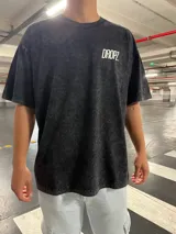 Remera negra con efecto lavado, de corte relajado y caída amplia. Presenta una estampa tipográfica "Hop On The Ride" en blanco y de gran tamaño en la espalda, y un mini logo "Dropz" en el pecho.