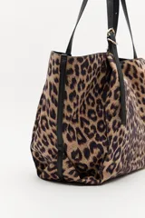 Cartera tipo shopper con estampado animal print, diseño amplio y flexible, con asas negras regulables y detalles metálicos.