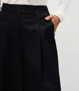 Pantalón pantacourt de sastrería con diseño amplio, cintura alta y pliegues frontales. Presenta piernas anchas, largo midi y cierre frontal discreto.