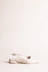Chatitas destalonadas de cuero charolado color beige con punta fina, taco bajo y detalle de tachas metálicas doradas alrededor del borde.