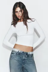 Jeans de tiro medio con diseño de cintura doblada, cinco bolsillos y cierre frontal con cremallera y botón metálico. Presenta un acabado desgastado con roturas en las rodillas y corte recto.