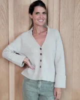 Cardigan de punto color beige, con escote en V, cierre frontal de botones y mangas largas con puños anchos acanalados.