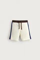 Short de baño blanco marfil con cintura marrón y cordón ajustable del mismo color. Presenta franjas laterales en tono azul marino con finos bordes rojizos y bolsillos laterales.