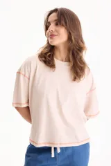 Remera oversize de algodón color beige, de manga corta, con costuras visibles en tono naranja contrastante y cordón ajustable en el dobladillo inferior.