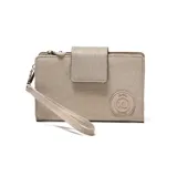 Billetera tipo fichero color beige, confeccionada en material textil con cierre de solapa y broche magnético. Incluye una correa de muñeca extraíble y un aplique circular con el logo de la marca en el frente.