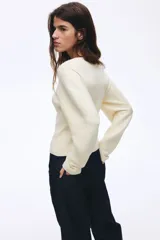 Saco ajustado en punto acanalado color beige, con cuello redondo, cierre frontal con botones jaspeados, hombros caídos y mangas largas con puños ceñidos.