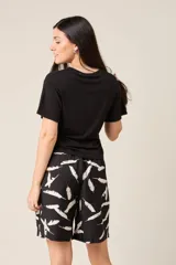 Bermuda de tiro alto con elástico fruncido en la cintura y bolsillos laterales. El tejido es verde oliva con un estampado de plumas blancas.