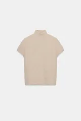 Top de punto color beige con cuello subido, manga corta y diseño texturizado con efecto arrugado. Presenta aplicaciones de perlas distribuidas en la parte frontal y las mangas.