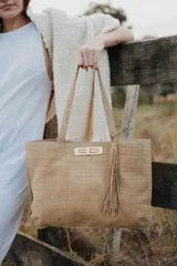 Cartera tipo tote de cuero con textura de reptil, color beige. Cuenta con doble asa de hombro, cierre frontal metálico y detalle de borla colgante en el lateral.
