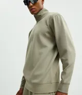 Buzo de cuello alto con cierre frontal parcial, manga larga y puños ajustados. Presenta un diseño minimalista en color verde militar.