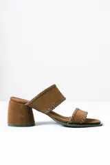 Sandalias tipo mule de taco medio ancho, confeccionadas en cuero gamuzado color marrón. Presentan dos tiras anchas con detalles de costuras pespunteadas en los bordes y punta cuadrada.