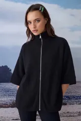 Poncho tejido de punto color negro, con cuello alto y cierre frontal completo. Presenta mangas de largo medio con terminación en puño acanalado y un diseño holgado.